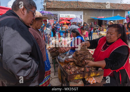 Woman selling fried meat at an open air stall. Very busy Sunday market in Tarabuco, department Sucre, Bolivia, Latin America Stock Photo