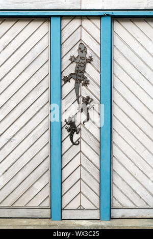 close up view of a white wooden door with blue siding and metal lizards as decoration Stock Photo