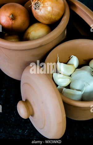 clay jars with onions and garlic  on a black granite table top ready for cooking Stock Photo