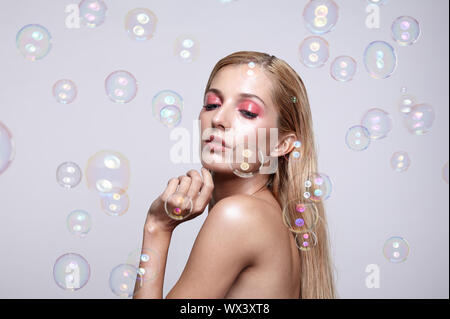 Beautiful young blonde woman with soap bubbles on grey background Stock Photo