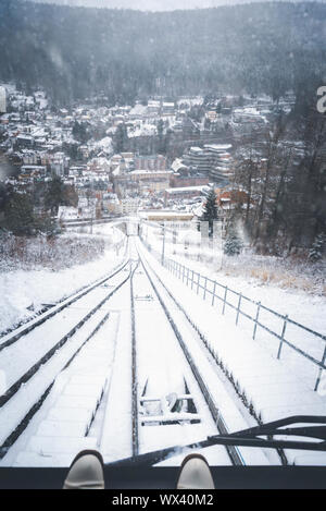 Traveling funicular railway vehicle and window view of the snowy railroad tracks, the snowy forest, and a snow-covered Bad Wildbad town, in Germany. Stock Photo