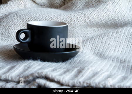Close up black cup with coffee on gray knitted sweater made of natural wool texture, wavy folds, selective focus Stock Photo