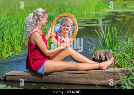 Young woman sitting with mirror at natural water Stock Photo