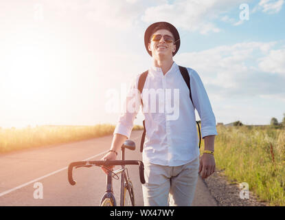 Young male cyclist walking by feet with a grass stalk in his mouth on a sunset background Stock Photo