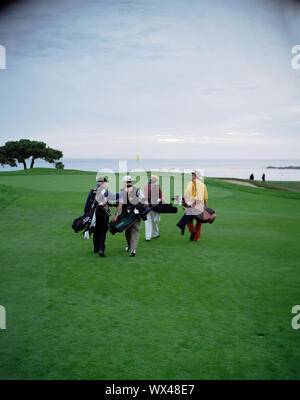 Four men carrying golf bags and walking across a golfing green. Stock Photo