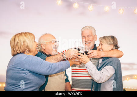 Happy senior friends cheering and toasting with red wine on terrace - Older people having fun at dinner party on patio at sunset Stock Photo