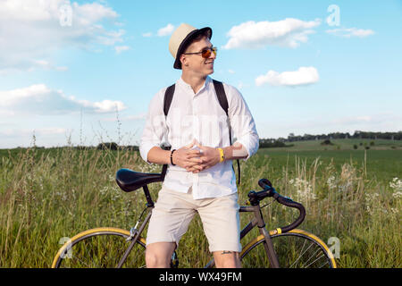 Young resting contented cyclist sitting on his bicycle during his stop on a countryside road Stock Photo