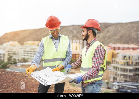 Workers engineers discussing about the new building area - Young builders reading the project in the construction site Stock Photo