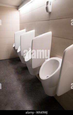 modern white ceramic urinals in a brown room Stock Photo