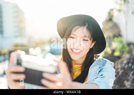 Happy Chinese influencer woman doing photo on vacation - Young trendy Asian girl taking selfie outdoor Stock Photo