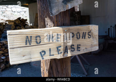 rusti wooden baord sign on a post with the warning no weapons written as instructions before enter Stock Photo