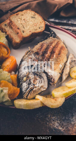 Grilled dorada fish with vegetables close-up. Vertical shot Stock Photo