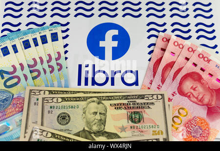 Facebook and Libra logos on the brochure surrounded by US Dollars, Euros and Chinese Renminbi banknotes. Conceptual photo. Stock Photo