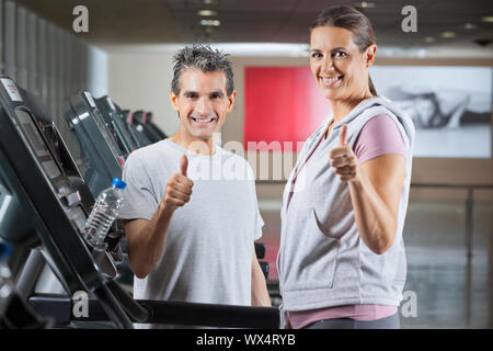 Happy mature instructor and female client showing thumbs up sign in health club - shallow depth of field, focus on trainer Stock Photo
