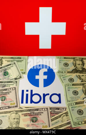 Facebook and Libra logos on the brochure which is covered by dollar notes and placed under the flag of Switzerland. Concept photo. Stock Photo