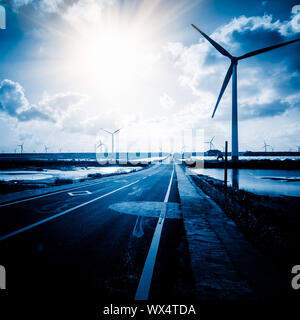Wind turbines on landscape along empty road against sky Stock Photo