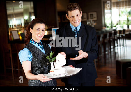 Here is cup of refreshing tea you ordered. Waitress holding tea tray as man pours Stock Photo