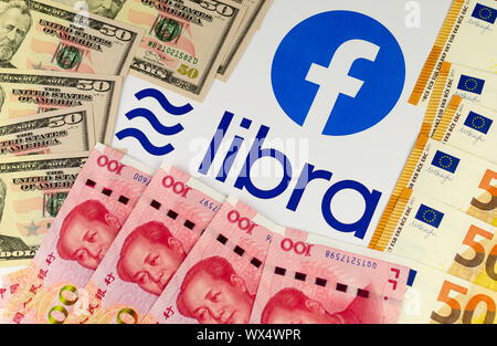 Facebook and its currency Libra logos on the brochure surrounded by US Dollars, Euros and Chinese yuan bills. Stock Photo