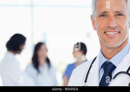 Doctor showing a beaming smile with his medical interns behind him Stock Photo