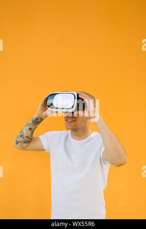 Virtual reality concept with man wearing VR glasses on orange background. Vertical outdoors shot. Stock Photo