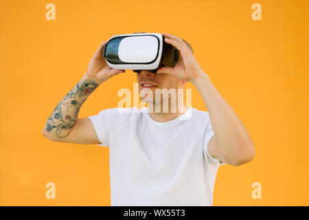 Tattoed man wearing virtual reality goggles in colored background. Smartphone using with VR headset. Horizontal shot. Stock Photo