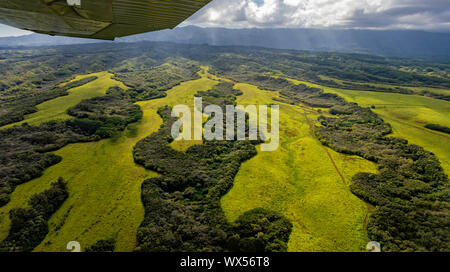 Aerial view from a fixed wing airplane of interior Kaui, Hawaii, USA near Lihue showing lush green meadows, tropical forests and the airplane wing Stock Photo