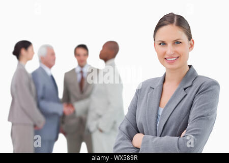 Smiling saleswoman with folded arms and colleagues behind her against a white background Stock Photo