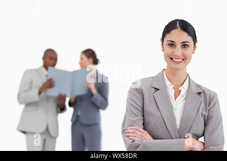 Smiling saleswoman with arms crossed and colleagues behind her against a white background Stock Photo