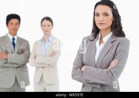 Confident saleswoman with arms folded and colleagues behind her against a white background Stock Photo