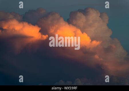 Cloudscape of fluffy storm clouds illuminated in hues of yellow, orange, pink, and purple by the light of sunset Stock Photo