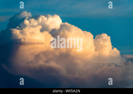 Cloudscape of dramatic white fluffy cumulus clouds illuminated by evening light contrasted with blue sky Stock Photo
