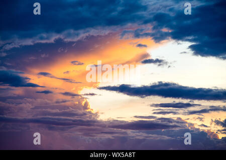Beautiful sunset illuminates dramatic cloudscape with storm clouds in hues of yellow, orange, and purple Stock Photo