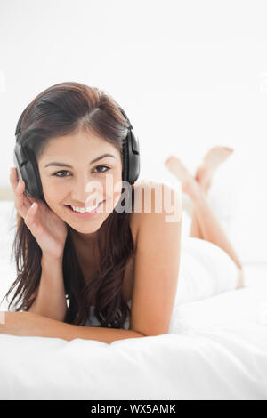 A close up picture of a  smiling woman with her headphones on, with her hand on them, while her legs are crossed. Stock Photo