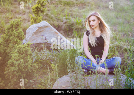 Pensive woman posing sitting on a stone. Stock Photo