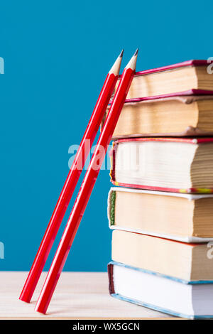 a stack of books and two red wooden pencils on a blue background, back to school concept Stock Photo