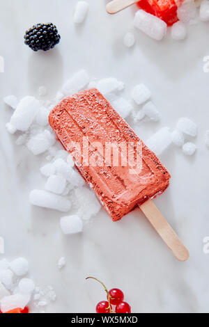 Berry black currant ice cream sorbet popsicles in color of the year 2019 Living Coral Pantone on crushed ice over a marble backg Stock Photo