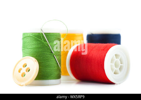 Four spools with green, red, yellow and blue threads, needle and button Stock Photo