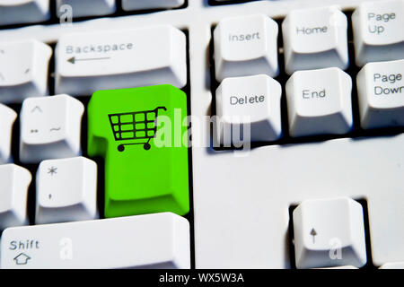 Computer Keyboard from a desktop computer with the enter key highlighted in green with a large shopping cart on it Stock Photo