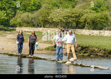 OGMORE BY SEA, WALES - APRIL 2019: People walking across the stepping stones across the River Ogwr in Ogmore by Sea in South Wales. One man has a dog Stock Photo