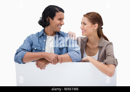 Smiling couple leaning on blank wall against a white background Stock Photo
