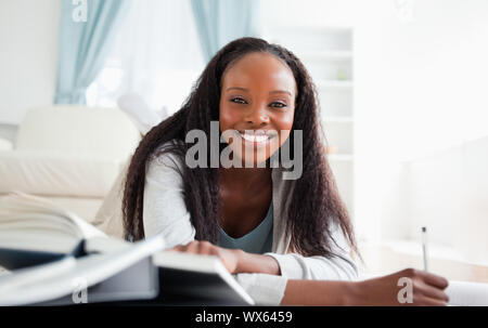 Smiling woman lying on carpet in living room doing her homework Stock Photo