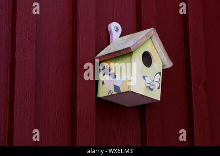 beautifully decorated birdhouse hung on a red wooden wall in Roback Stock Photo