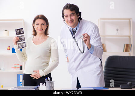 Old pregnant woman visiting young male doctor Stock Photo