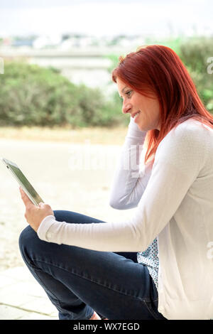 Portrait of a pretty expressive redhead woman reading information on its touch pad Stock Photo
