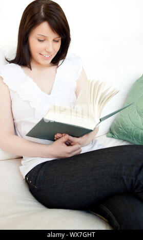 Concentrated woman reading a book sitting on a sofa at home Stock Photo