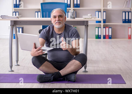 White bearded old man employee doing exercises in the office Stock Photo