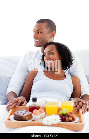 Enamoured Afro-american couple having breakfast lying on their bed Stock Photo