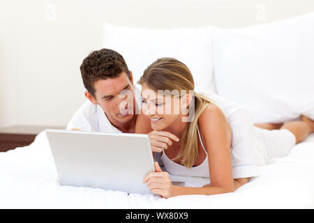 Affectionate couple using a laptop lying on their bed Stock Photo