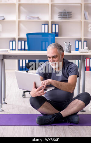 White bearded old man employee doing exercises in the office Stock Photo