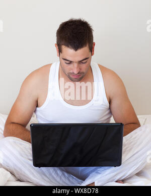 Handsome  man using a laptop in his bedroom Stock Photo